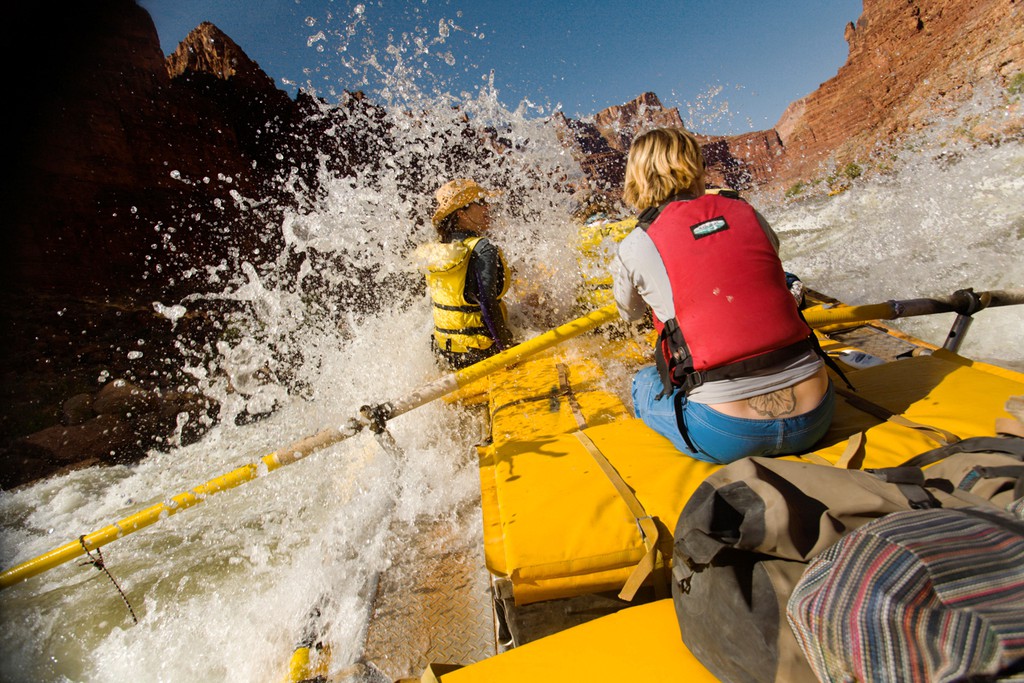Rafters punching through rapids on a river in a canyon.
