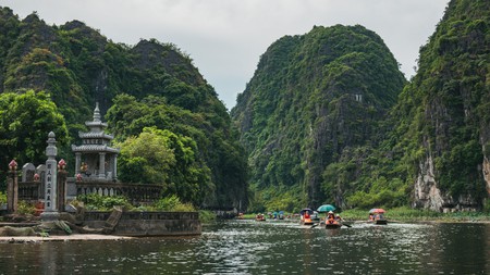 Tourists in boats row up the Ngo Dong River through limestone mountains and caves in Tam Coc, Ninh Binh Province