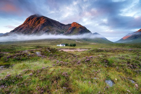 Stunning sunrise over a cottage beneath the mountains at Glencoe in the Scottish Highlands
