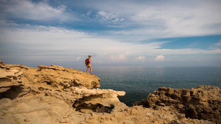 A hiker standing on top of rocks looking out at a blue sea
