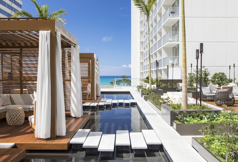 The sleek infinity pool with in-pool lounge chairs and ocean views at 'Alohilani Waikiki Beach