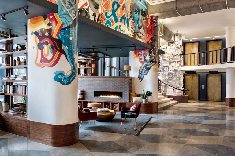 Graffiti-laden walls of a lobby lounge area at The Revolution Hotel with velvet chairs, bookshelves and a fireplace