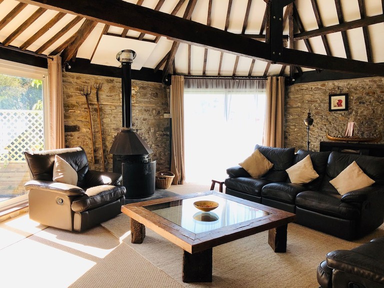 Converted barn with wood-beam ceilings, stone walls, leather furniture and freestanding stove at Helscott Barns in Bude