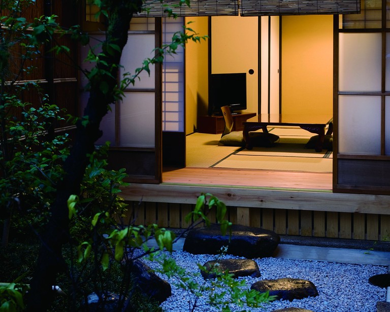 A low table and flat-screen TV inside Kyoto Machiya SHOUAN, Kyoto, as viewed from its private outdoor garden; sliding shōji doors separate the spaces