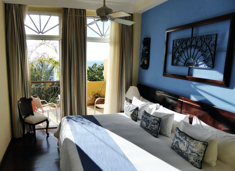 Deluxe Room at Casa do Amarelindo with blue walls and well-designed furniture, with a balcony overlooking the sea