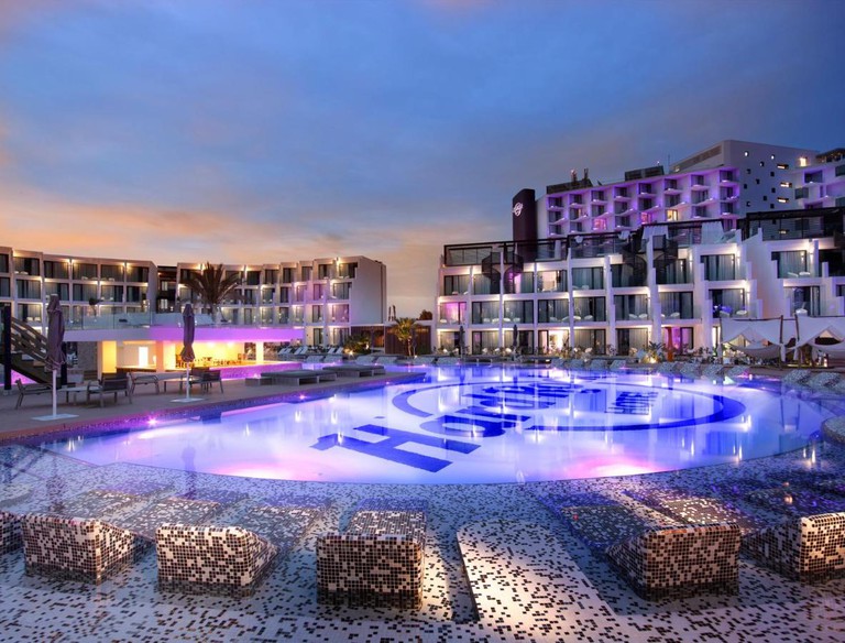Logo-imprinted half-circle outdoor swimming pool lit up at night at Hard Rock Hotel Ibiza, Balearic Islands