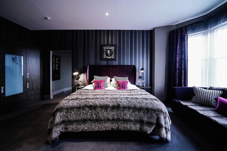 Sultry bedroom in violet hues with plush velvet furnishings, dark striped wallpaper and soft carpet at Malmaison Dundee
