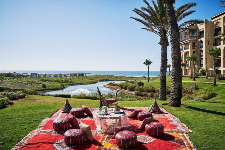 Several cushions and small seats on a rug on a lawn with sea views outside Mazagan Beach and Golf Resort