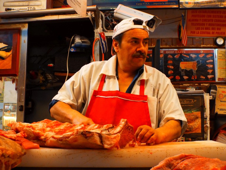 A butcher in a red apron cuts up some meat at Mercado Medellin