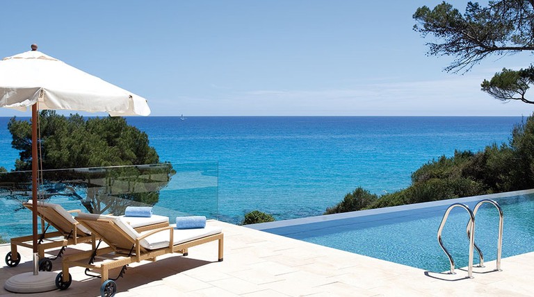 Two luxury sun loungers under a parasol next to an infinity pool overlooking the Mediterranean Sea at Can Simoneta