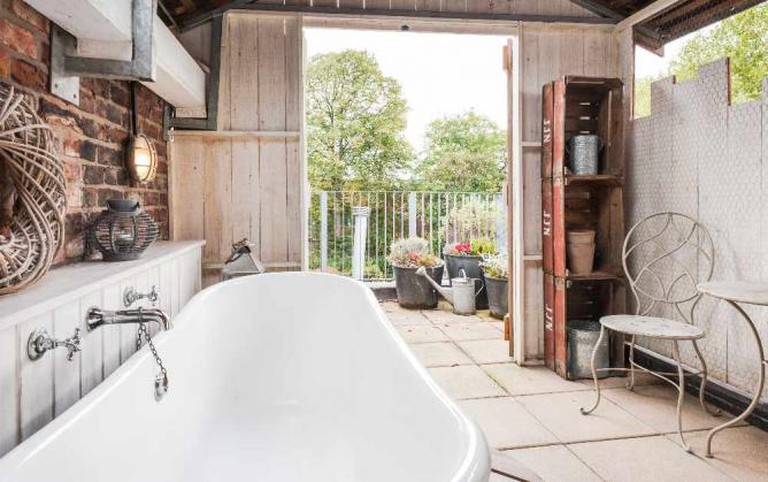 Rustic looking bathroom at Eleven Didsbury Park with roll top bath, exposed brick walls and doors leading to outside