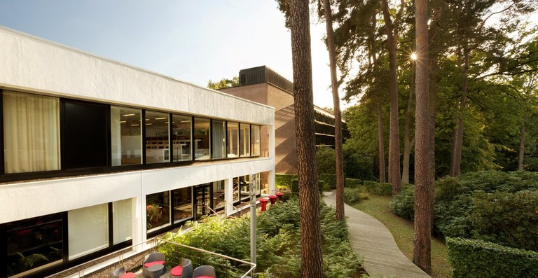 An outside view of the cream and modern building with large windows at Dolce La Hulpe, with trees opposite