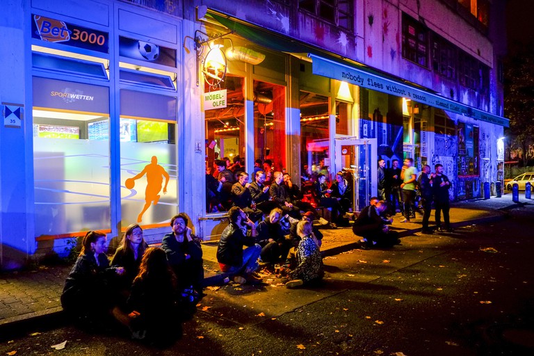 Young people sit at the roadside in front of the bar Mobel Olfe in Berlin.
