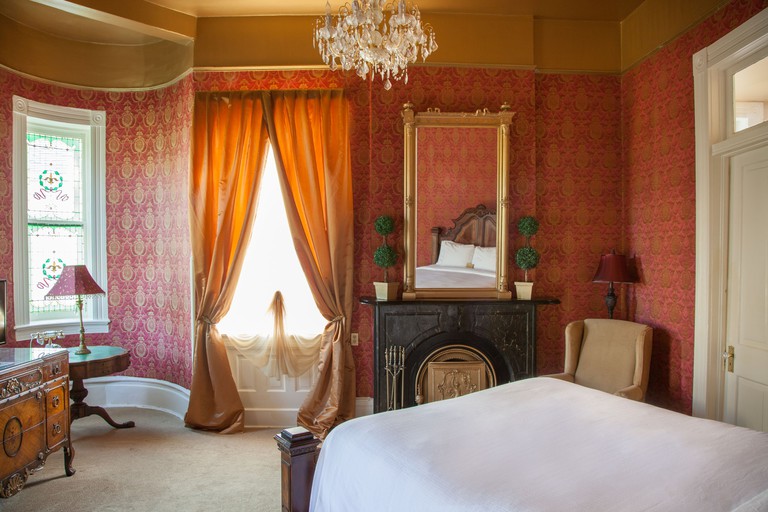 A bed, fireplace, and window with drapes in a hotel room at the Cornstalk Hotel