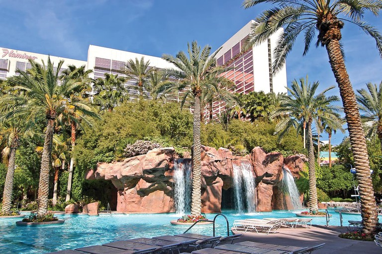 The outdoor pool, with a rock grotto and waterfalls, and several palm trees, at Flamingo Las Vegas