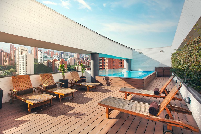 Wood lounge chairs on a wood rooftop deck with small dipping pool and panoramic city views at Sites Hotel