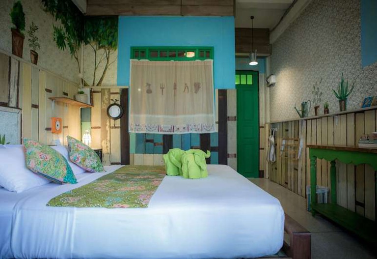 Green towels folded into an elephant shape on a double bed in a plant-themed room at Phranakorn-Nornlen Hotel