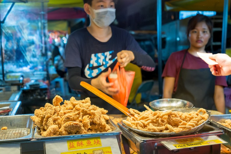 Night market vendor packing battered fried Fish 'n Chips and cuttlefish for buyer at Kuala Lumpur, Malaysia