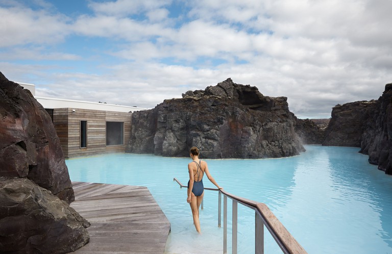 A woman enters the geothermal pool surrounded by rocks at the Retreat at Blue Lagoon in Grindavík, Iceland