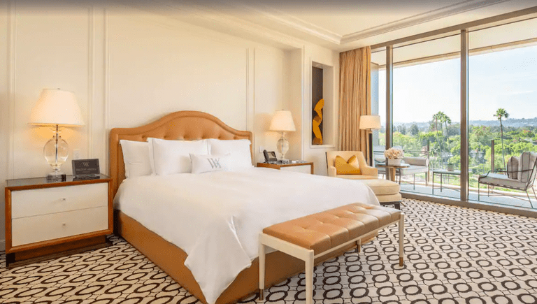Luxury bedroom in white and caramel hues with balcony offering panoramic views at the Waldorf Astoria Beverly Hills