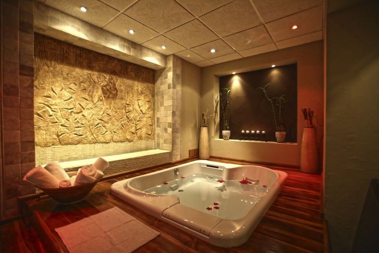 An indoor jacuzzi with rose petals, calm lighting and a basket of towels at The Spa Royal Sands