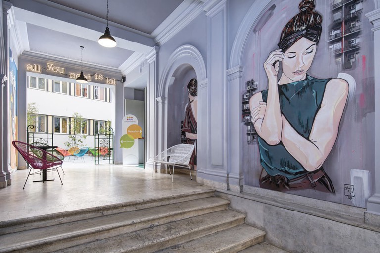 Artwork of a woman on the wall and seating in the entrance at RomeHello Hostel
