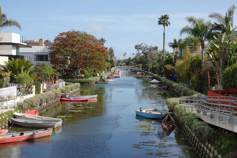 Venice, CA / USA - March 23, 2019: Small boats, homes, and a bridge crossing the water in the Venice Canal Historic District are shown during the day.