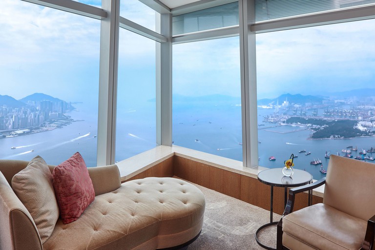 A top-floor corner seating area with the waterfront and the city visible from the windows at The Ritz-Carlton Hong Kong