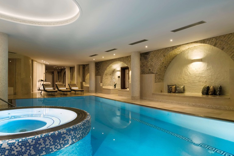 The indoor pool area at Grand Hotel Kempinski Vilnius with loungers and bare brick niches