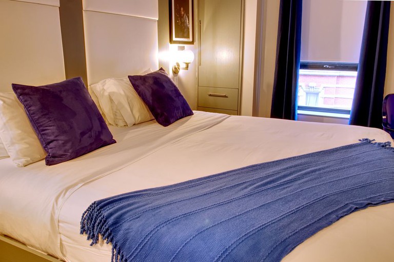 Double bed with white bedding and purple decorative pillows at The Ridge Hotel