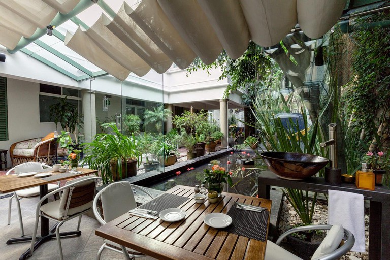 An open-air dining space at Hotel Villa Condesa with a rectangular pond, wooden tables and lots of greenery