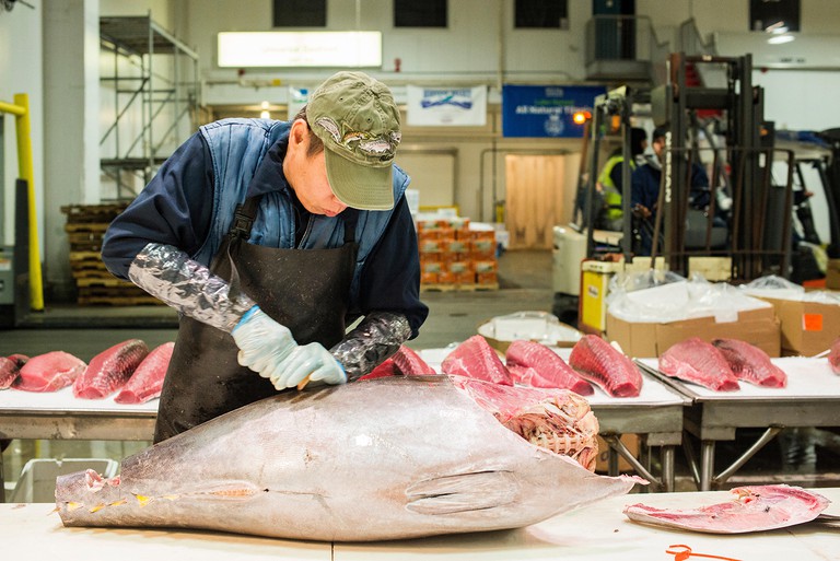 New York City, USA. Wholesale market stall employee cutting up a fresh tuna fish at the New Fulton Fish Market, Hunts Point, The Bronx.