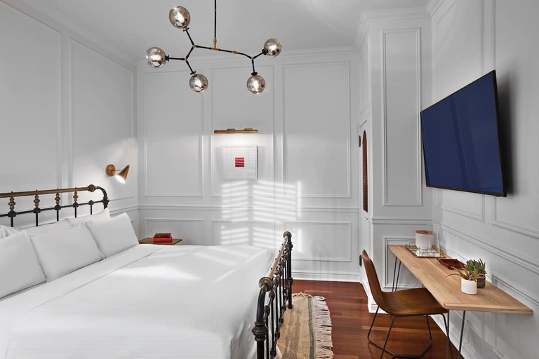An iron-framed bed in a white wood-panelled hotel room in Manhattan.
