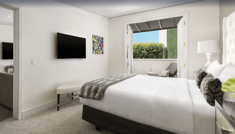 Chic bedroom in white and grey tones with plantation-style doors to shaded terrace in suite at Mosaic Hotel, Beverly Hills
