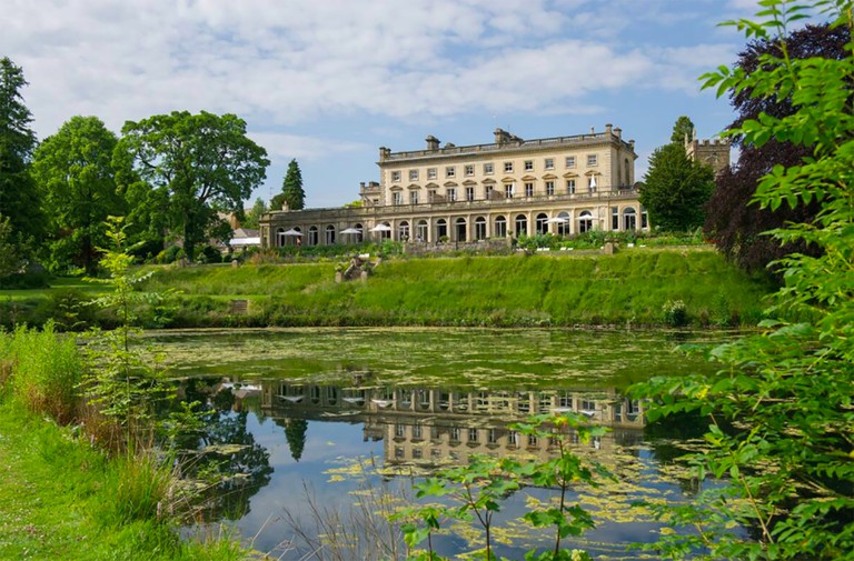The exterior of Cowley Manor near Cheltenham, as viewed from an adjoining lake.