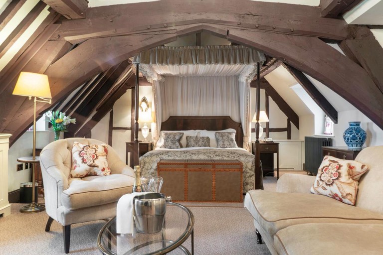 A bedroom with four-poster bed and two chairs at Ellenborough Park in the Cotswolds