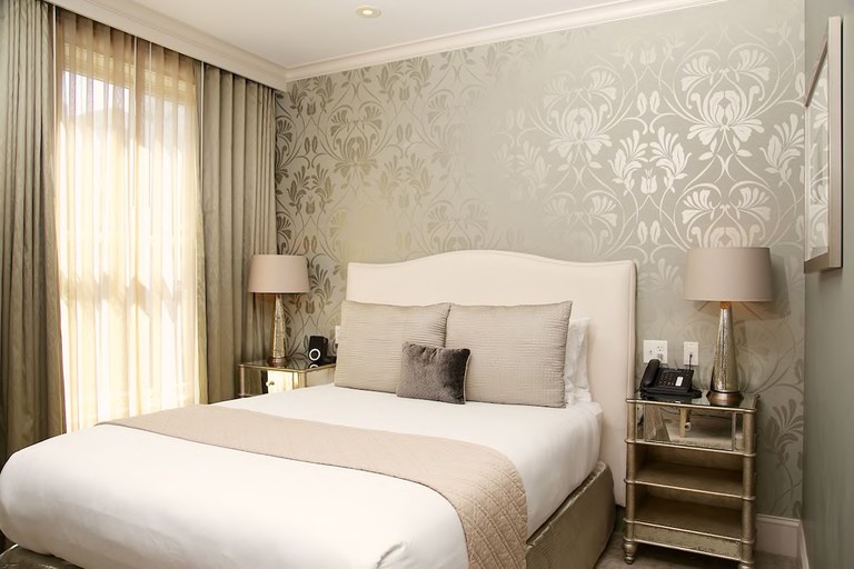 A stylish bedroom at Hotel Veritas, with a cushioned bed, lamps, bedside tables and windows