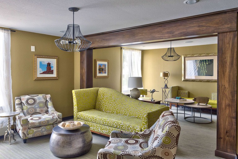 Quirky seating area in a room at 816 Hotel, with dark beige walls, a patterned lime-green couch, patterned armchairs, gray hardwood floors, a wooden arch framing an entryway and modern light fixtures