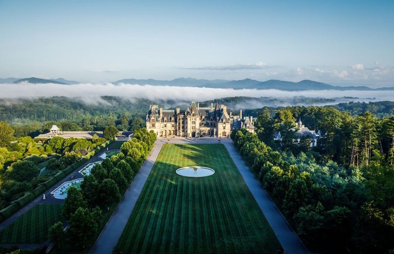 The Biltmore Estate with a manicured front lawn leading to a Châteauesque mansion, behind which is the Blue Ridge Mountains