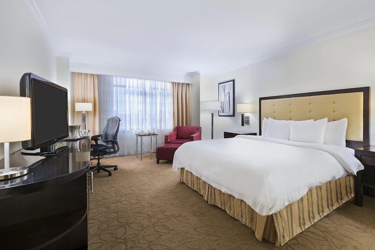 A traditional one-bed guest room in shades of brown and with a red armchair at the Hilton Richmond Hotel & Spa