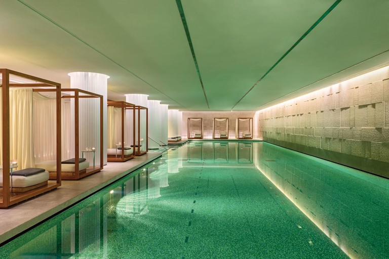 The long indoor pool lit by underwater lights and gauze columns between the rows of cabanas at the Bulgari Hotel in London.