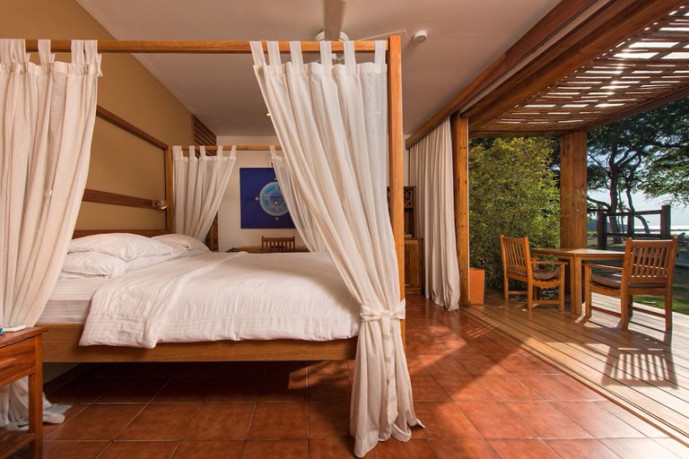 A four-poster bed leading to an open terrace with a table and chairs in a hotel room at Hotel Capitán Suizo /