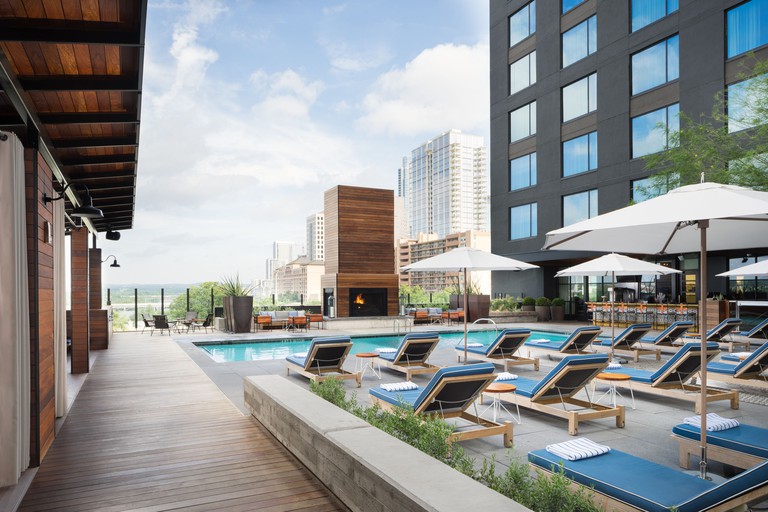 A rooftop pool with blue-cushioned lounge chairs and seating area with fireplace at the Kimpton Hotel Van Zandt, Austin