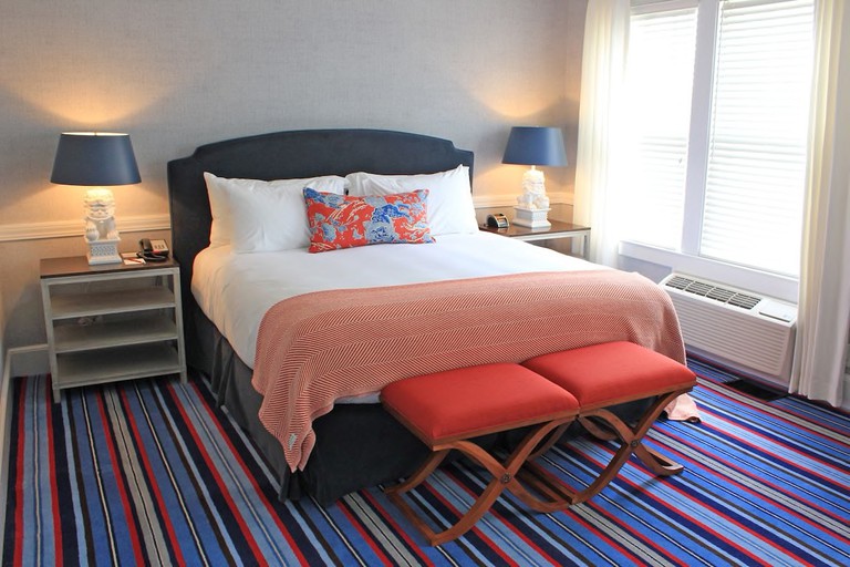 A bedroom with a pillowy bed, striped carpet, two bedside tables and navy blue lamps and windows at Kennebunkport Inn