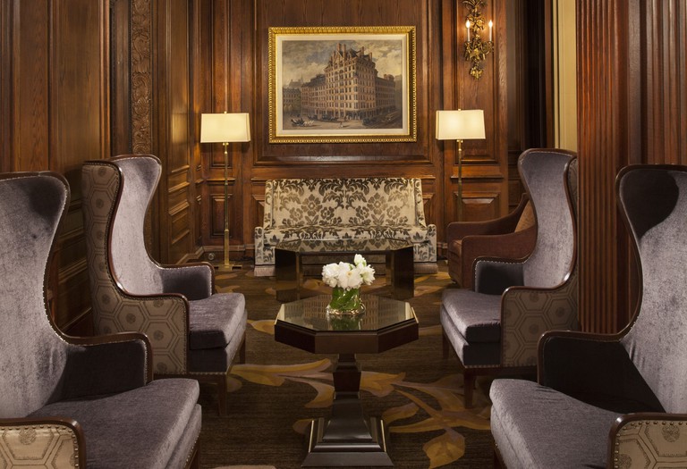 A cosy lounge at Omni Parker House, with armchairs, a coffee table with flowers, a picture on the wall and lamps