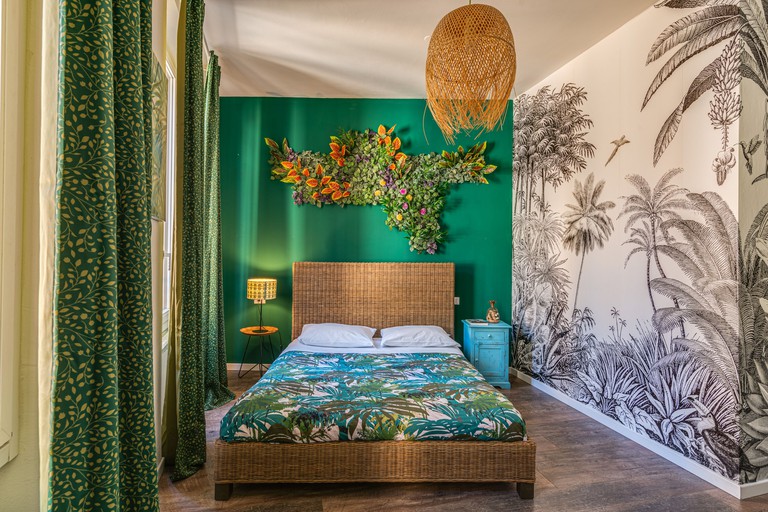 Tropical-themed room with jungle wall mural, green accent wall, leaf-patterned curtains and floral art piece at Code Rooms, Florence