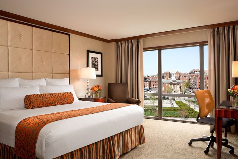 Deluxe room in warm tan and pumpkin hues with desk, ergonomic chair and floor-to-ceiling windows at the Bostonian Boston