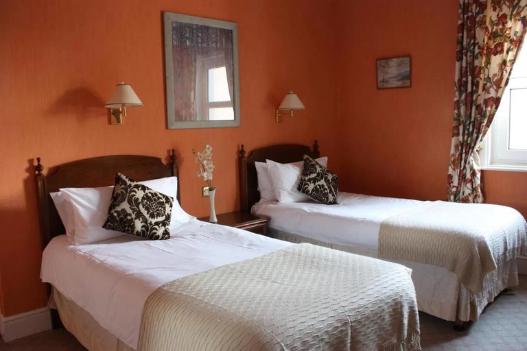 Two single beds separated by a bedside table in room with orange painted walls at 17 Wilmington Square