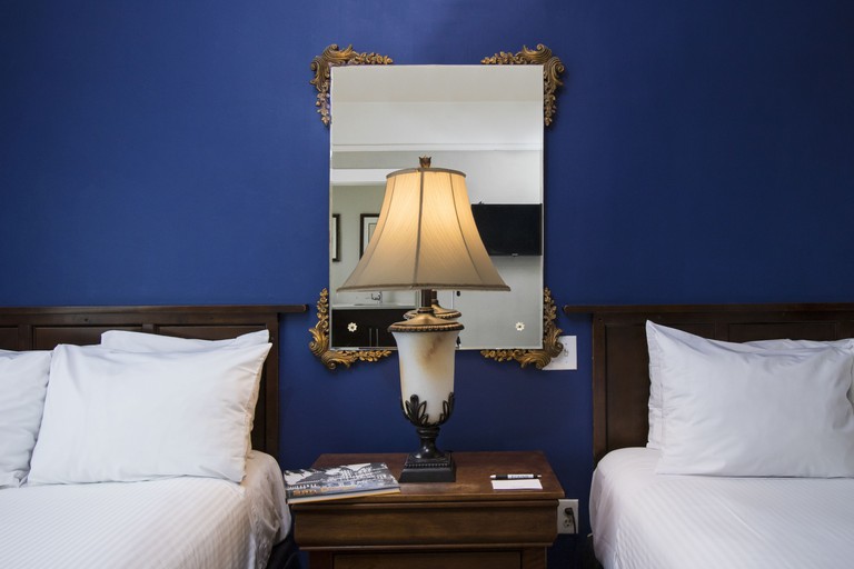 Close-up view of nightstand between two beds with decorative lamp and mirror against midnight blue wall at FOUND Hotel San Diego