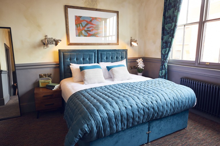 Double bed with blue velvet headboard in room with mirror and radiator at Frederick Street Townhouse